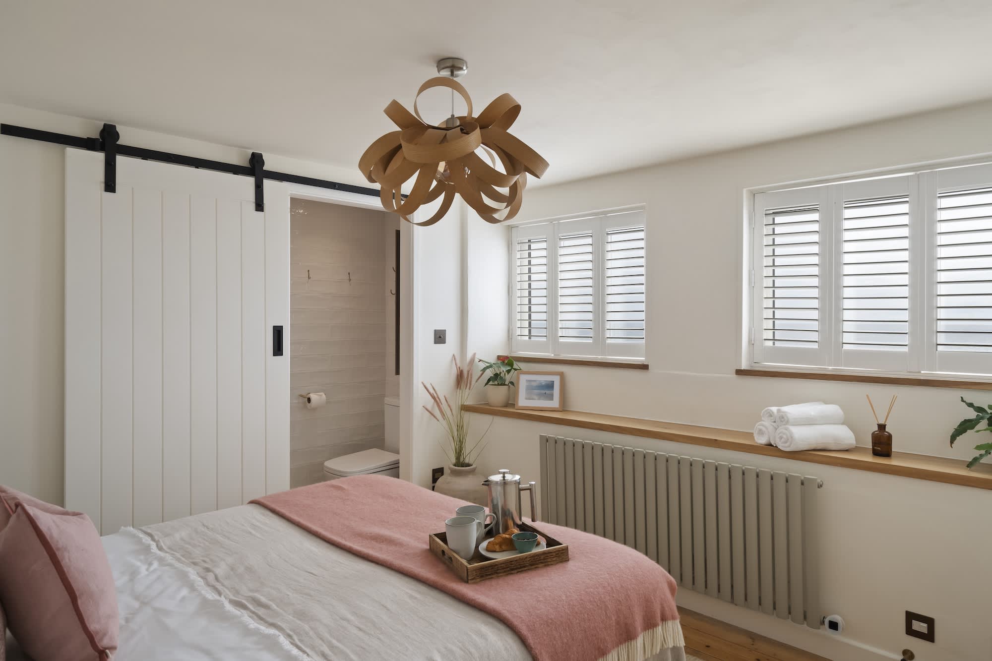 King bedroom with panelled barn door and soft pink linen at Triton, Porthleven