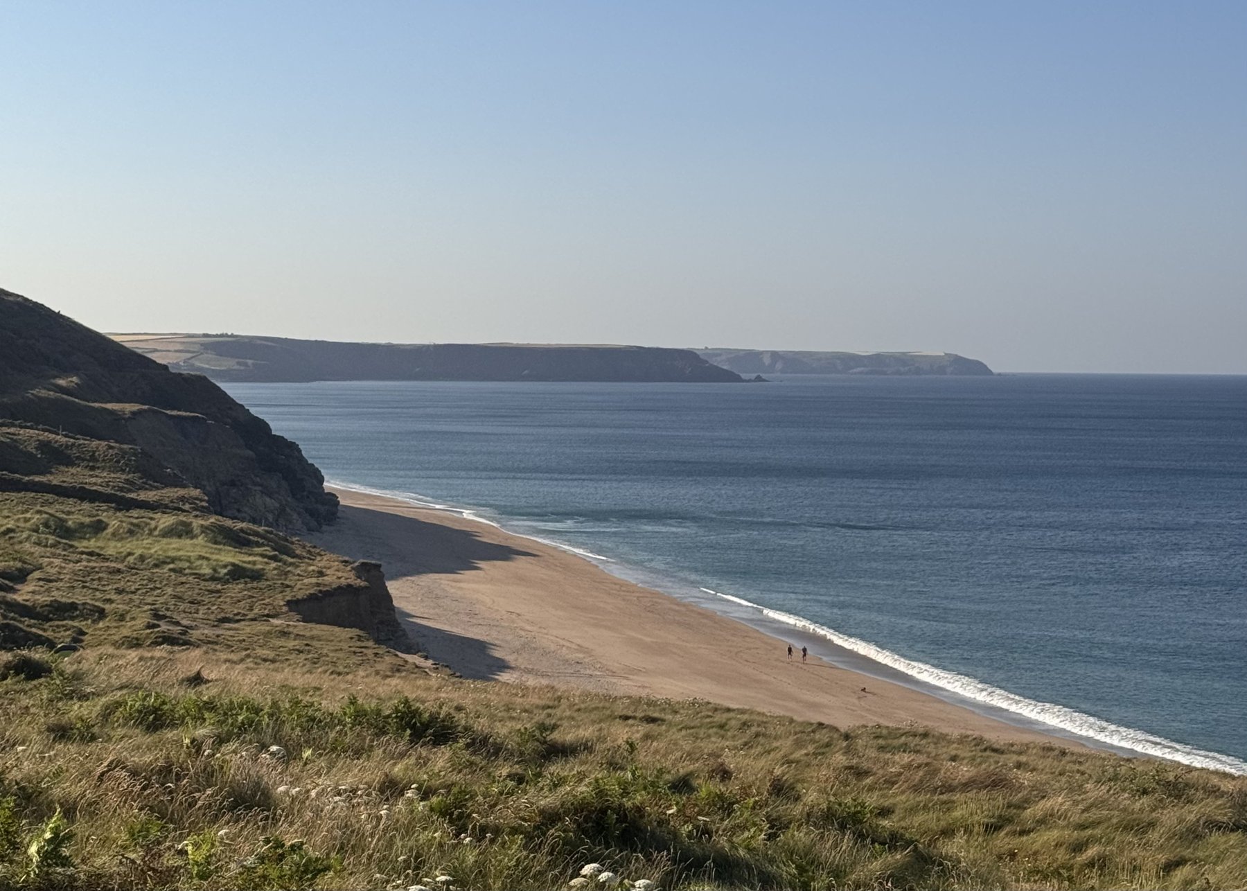 Empty sand and turquoise water below the coast path west of Porthleven